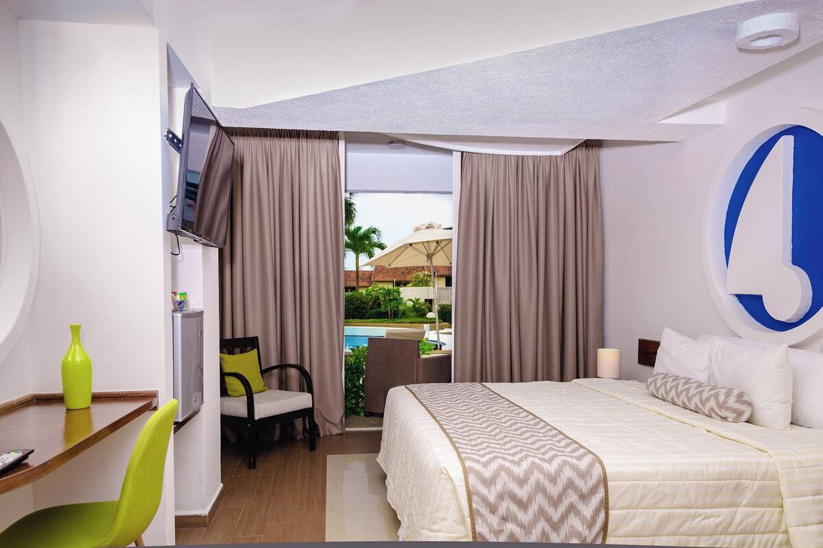 Habitación de hotel con cama, escritorio, silla, televisión y vista a una piscina.
