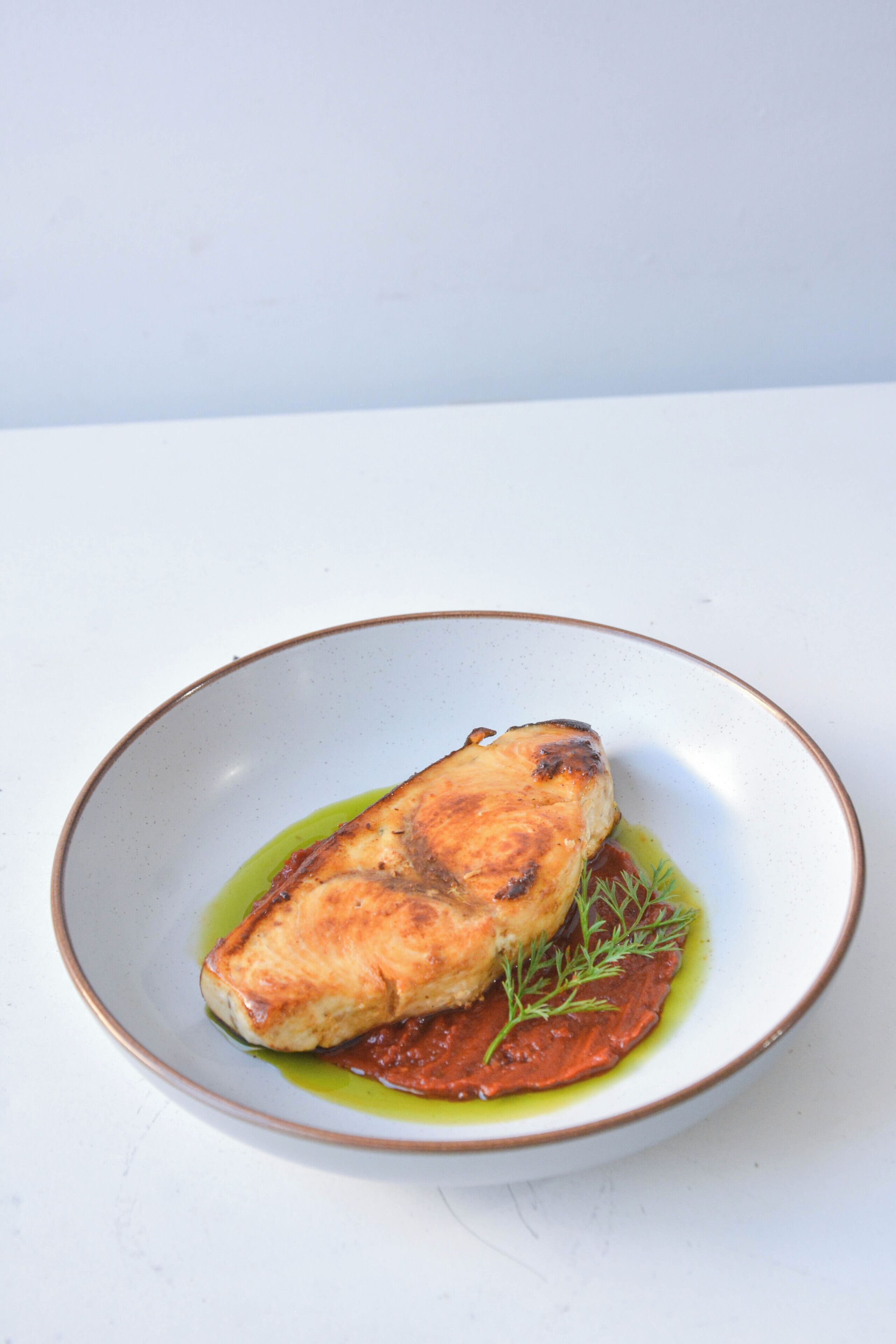 A plate with a piece of grilled fish, a green sauce, and a garnish.