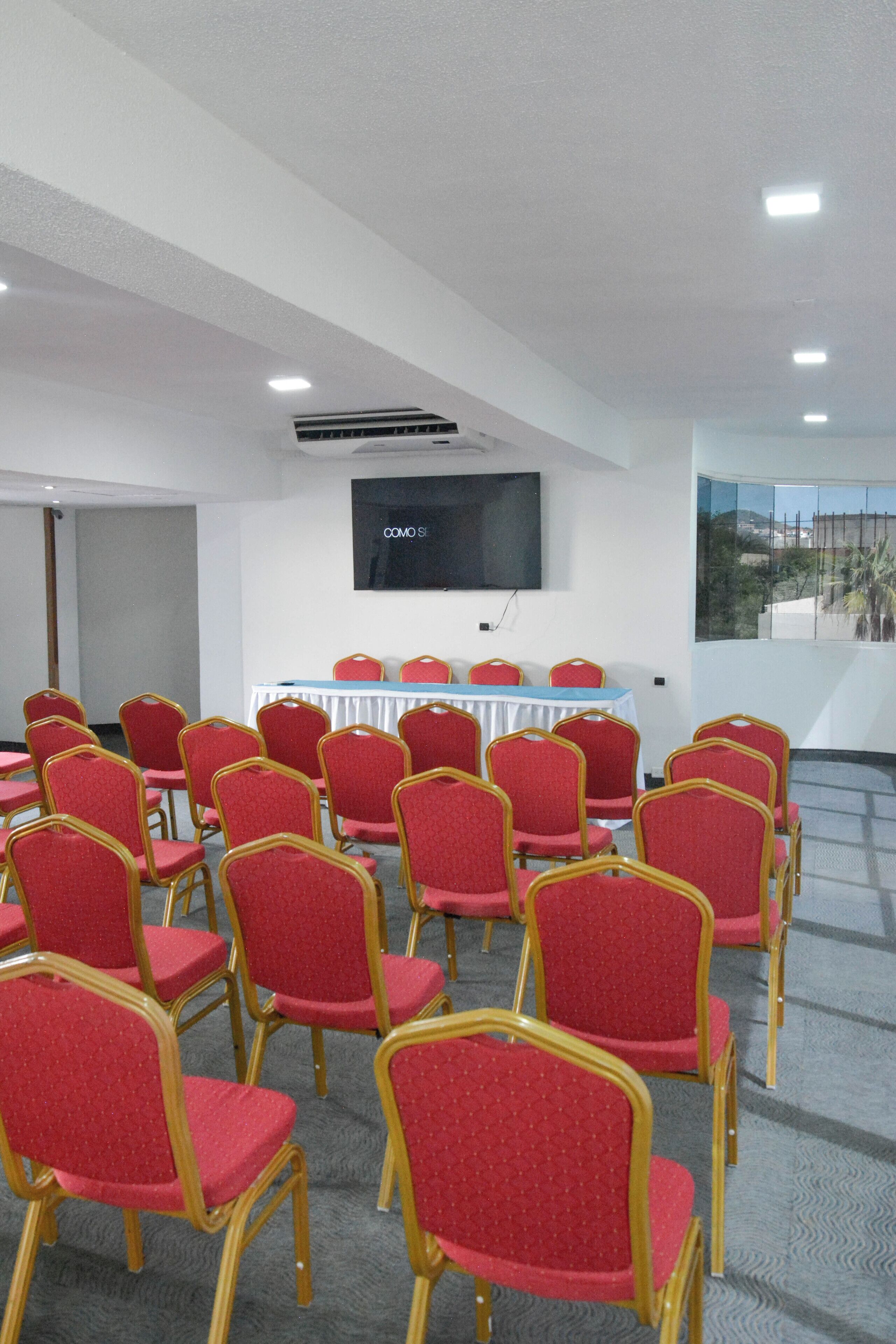 A conference room with rows of red chairs, a table with a blue tablecloth, and a mounted TV screen.