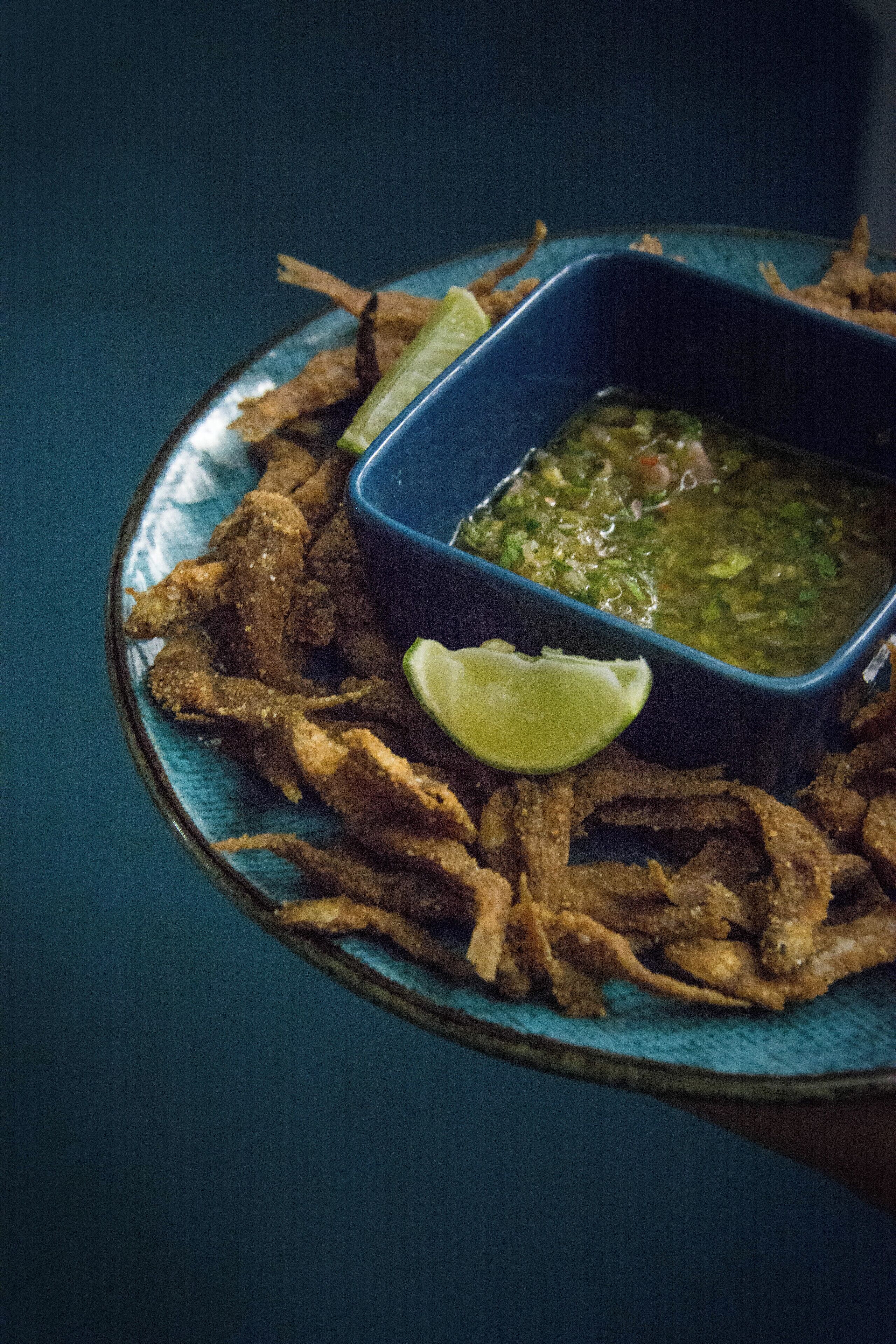 A plate of fried food with a lime wedge and a bowl of green sauce.