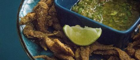 A plate of fried food with a lime wedge and a bowl of green sauce.