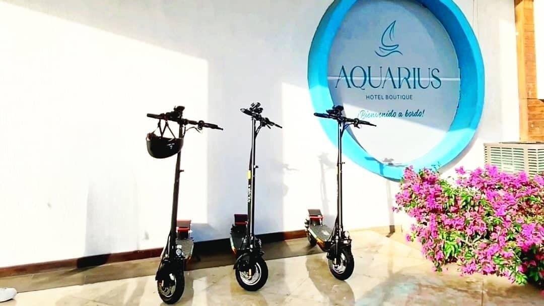 Drei Elektroroller sind vor einer Wand mit dem Schild "AQUARIUS HOTEL BOUTIQUE" abgestellt.
