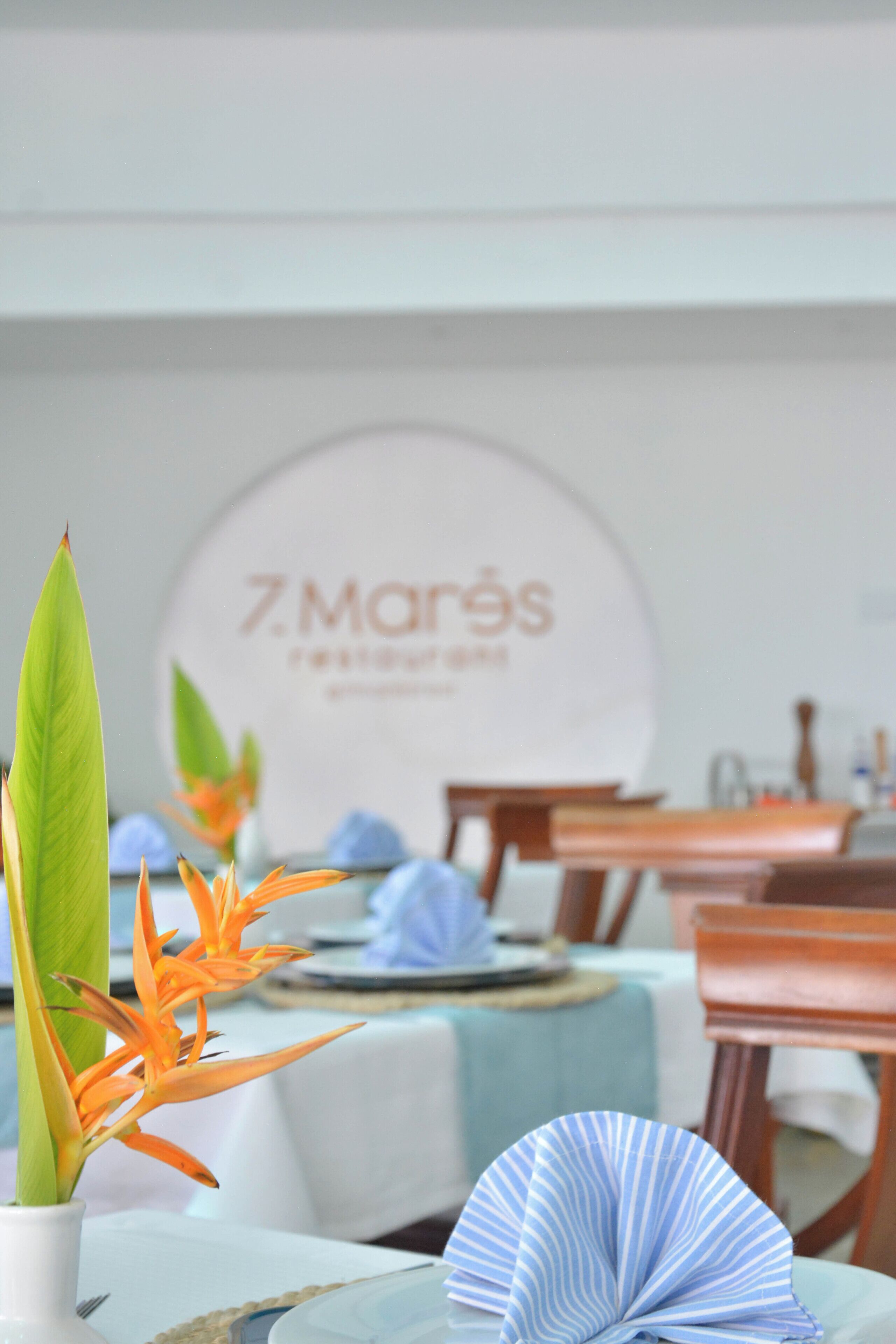 A dining area with tables set for a meal, a sign in the background, and a decorative plant.