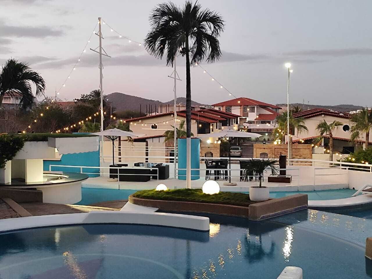 Área de piscina en un complejo turístico, con varias piscinas, sillas de descanso y sombrillas.