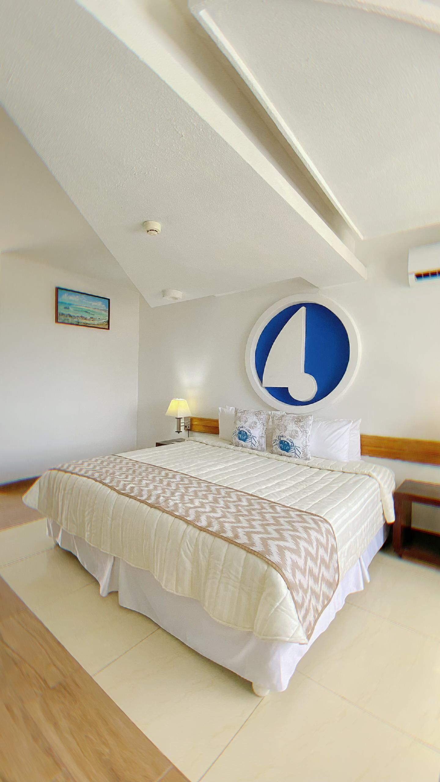 A hotel room with a large bed, a round wall decoration, a nightstand, and a painting on the wall.