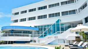 A modern hotel with a pool, a covered area, and a staircase leading to the upper floors.