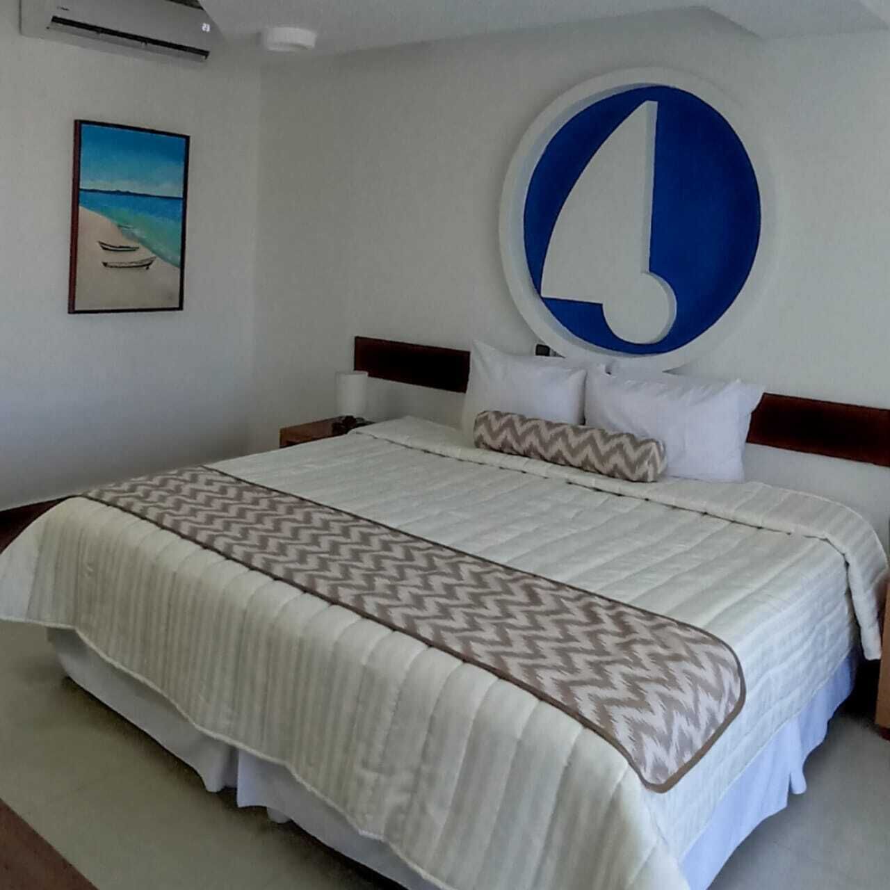 A hotel room with a large bed, a headboard with a circular design, and a painting of a beach scene on the wall.