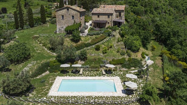 A stone house with a swimming pool surrounded by greenery.