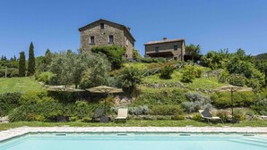 A pool area with lounge chairs and umbrellas, a stone building, and lush greenery.