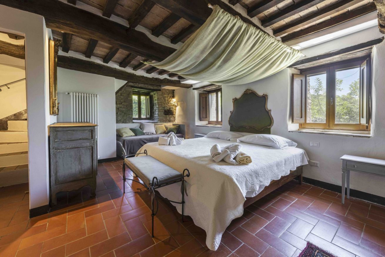 A bedroom with a bed, a bench, a radiator, a window, and a stone wall.