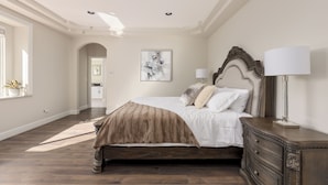 A bedroom with a large bed, a nightstand, a lamp, and a painting on the wall.