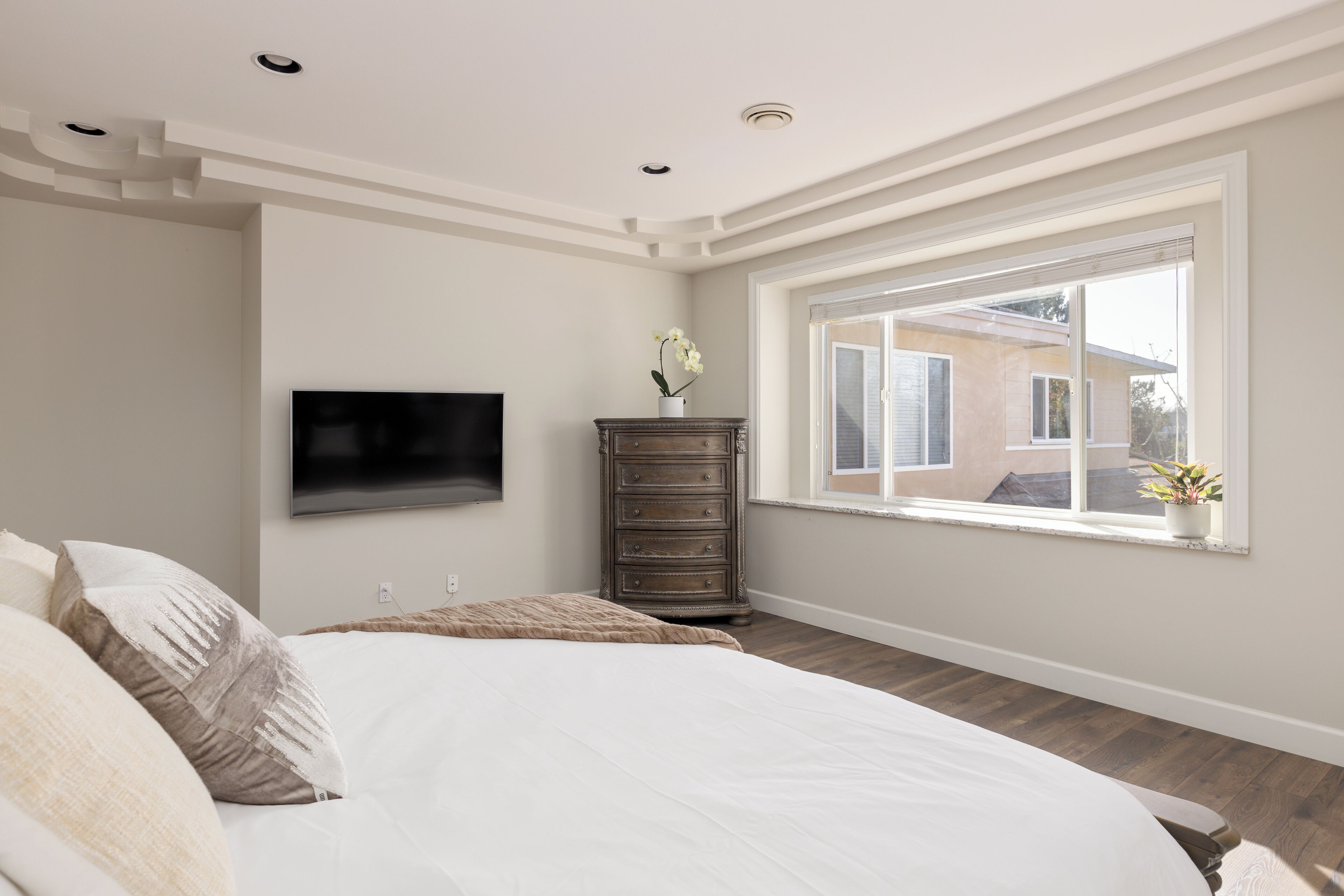 Ein Schlafzimmer mit einem Bett, einer Kommode, einem an der Wand montierten Fernseher und einem Fenster mit Blick ins Freie.