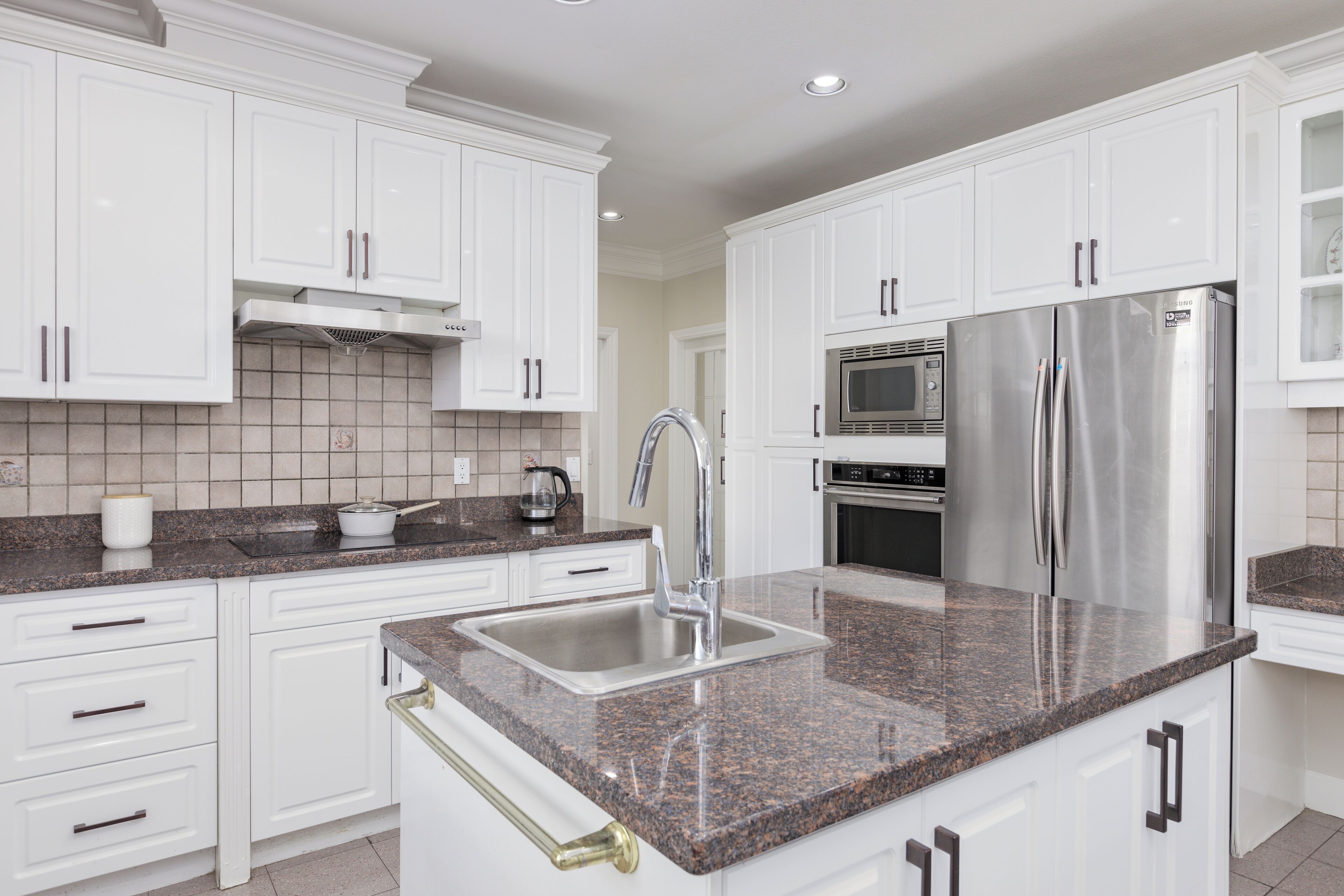 A modern kitchen with white cabinets, stainless steel appliances, granite countertops, and a double sink.