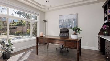 A spacious room with a large window, a wooden desk, a chair, a potted plant, and a bookshelf.
