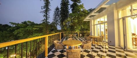 A terrace with a checkered floor, outdoor seating, and a view of trees.