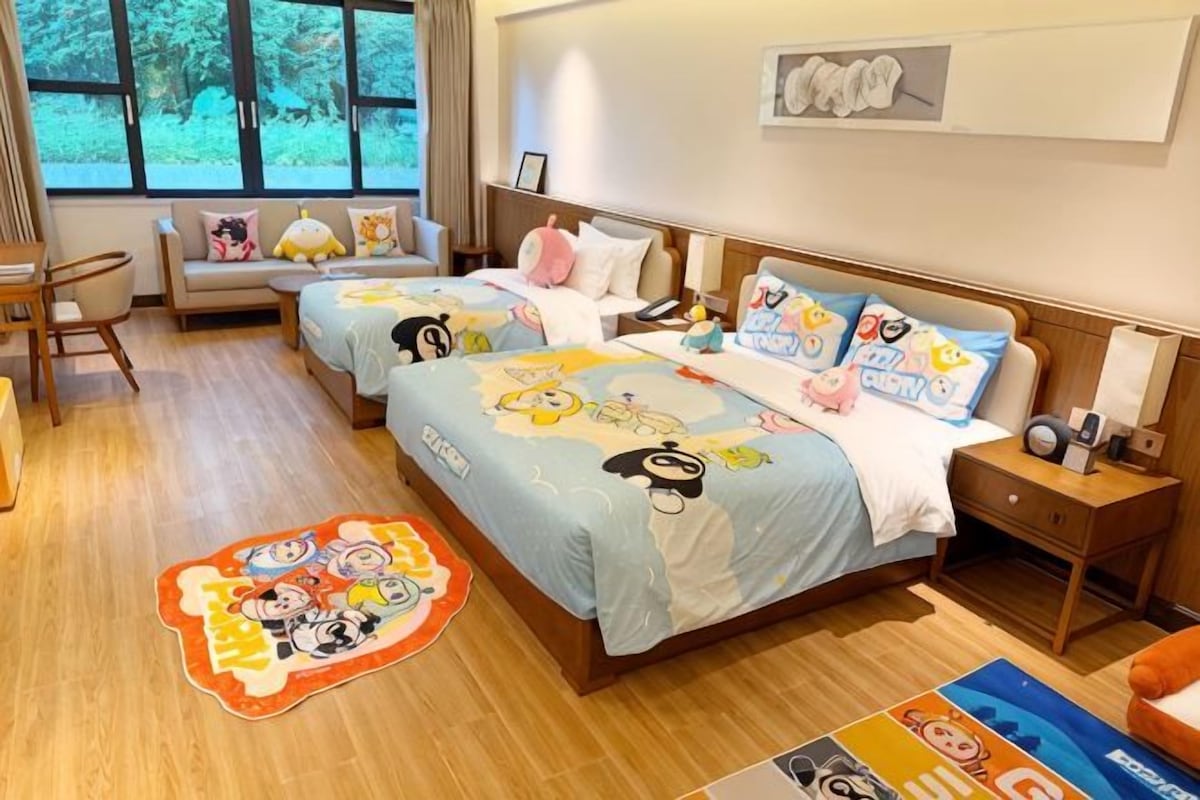 Une chambre d’hôtel avec deux lits, un canapé, un bureau et une fenêtre donnant sur les arbres.