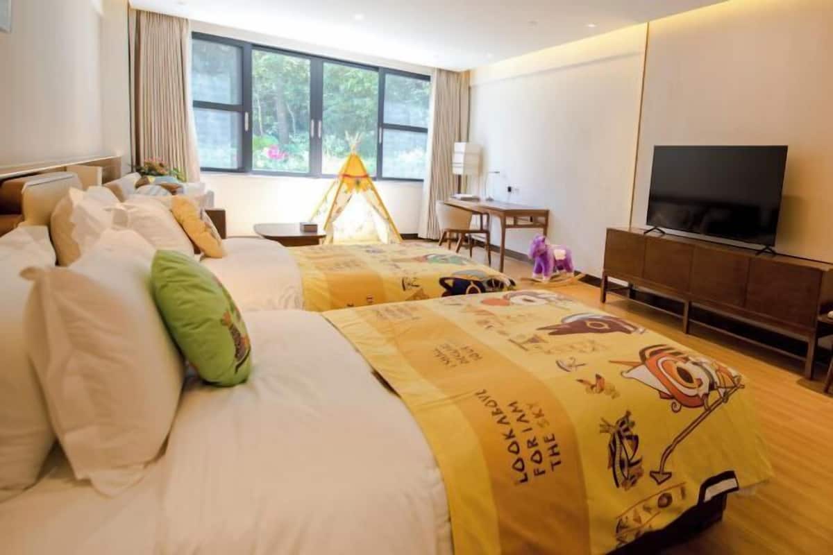 Une chambre d’hôtel avec deux lits, une télévision, un bureau et une fenêtre donnant sur un espace verdoyant.