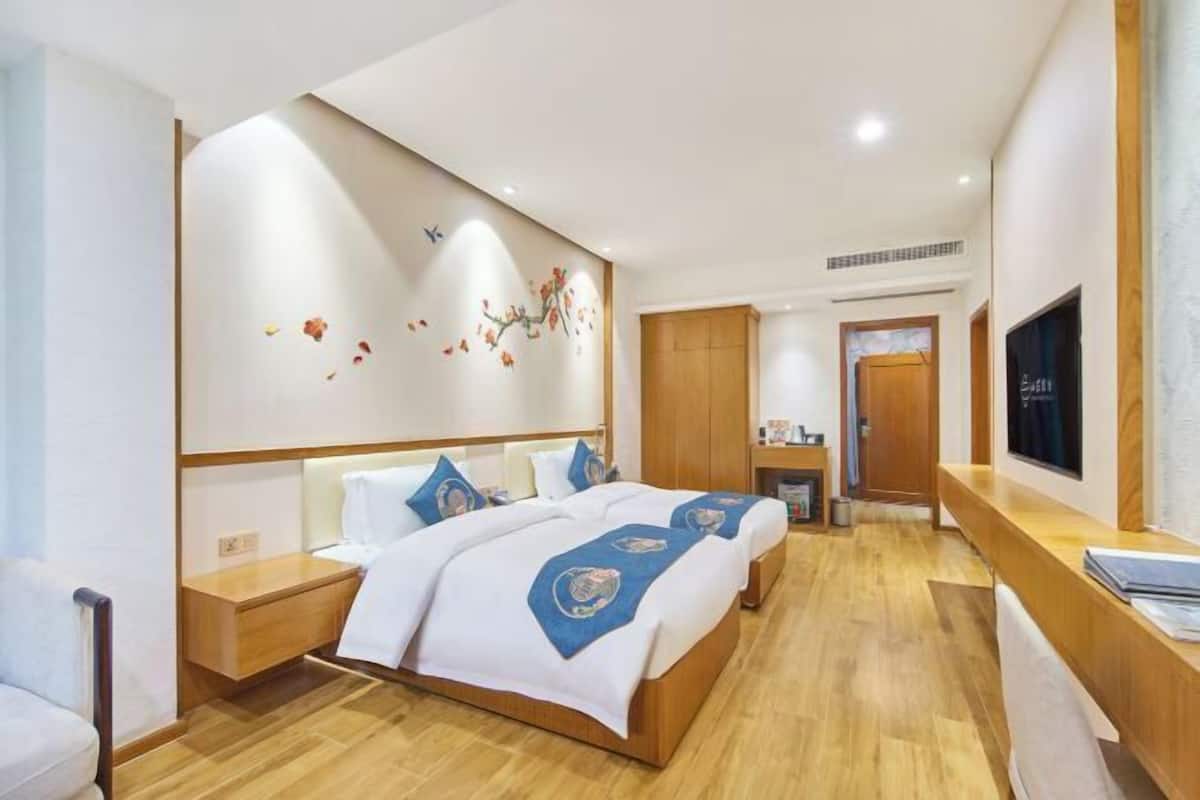 Une chambre d’hôtel avec un grand lit, une tête de lit en bois, un bureau avec une chaise, une télévision et une œuvre d’art accrochée au mur.