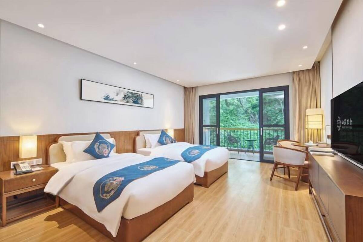 Une chambre d’hôtel avec deux lits, un bureau et une grande fenêtre donnant sur un paysage verdoyant.