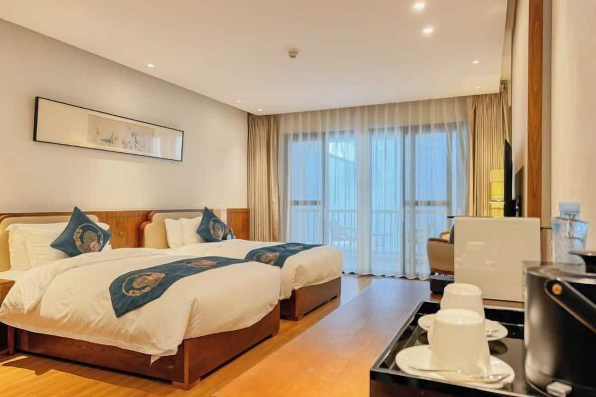 Une chambre d’hôtel avec deux lits, un bureau avec une machine à café et une grande fenêtre avec des rideaux.