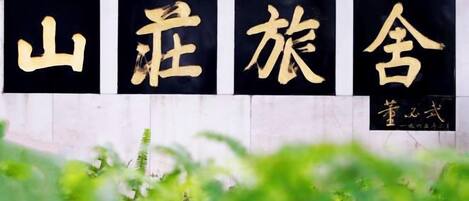 A wall with large black and gold characters, likely a name or title, and a smaller inscription below.