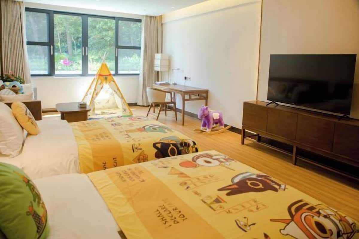Une chambre d’hôtel avec deux lits, un bureau, une télévision et une fenêtre donnant sur un paysage verdoyant.