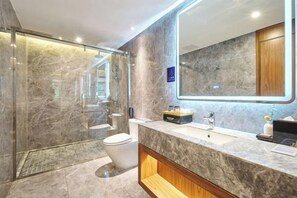 Un baño moderno con ducha envuelta en vidrio, tocador de mármol y un espejo grande.