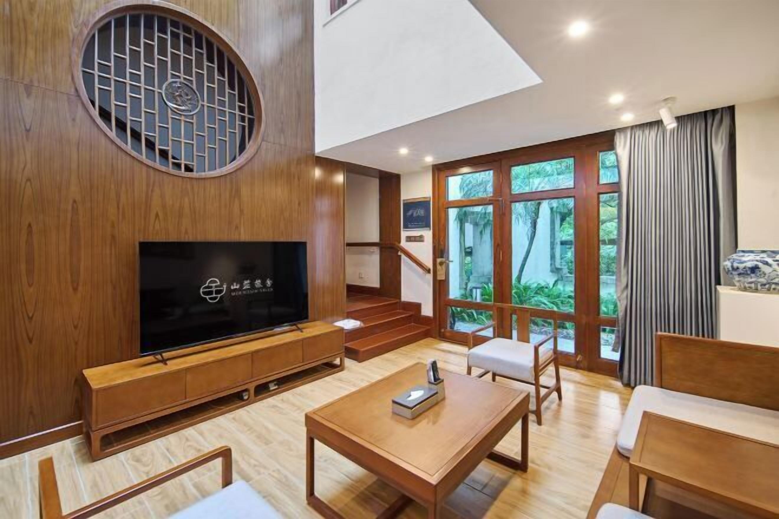 Uma sala de estar moderna com televisão de tela plana, móveis de madeira e uma janela grande com vista para o verde.
