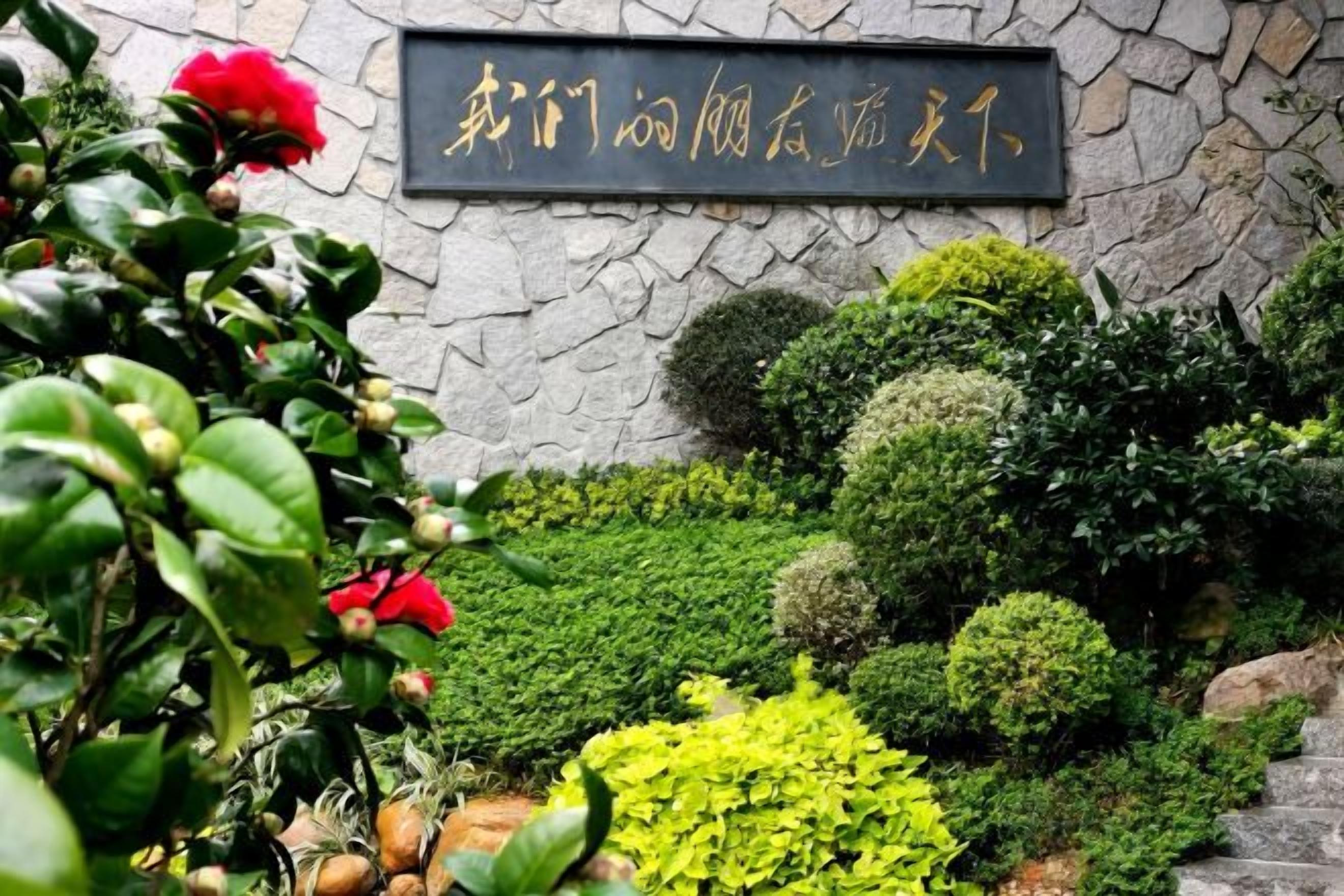 A stone wall with a sign, surrounded by well-maintained greenery and a variety of plants.