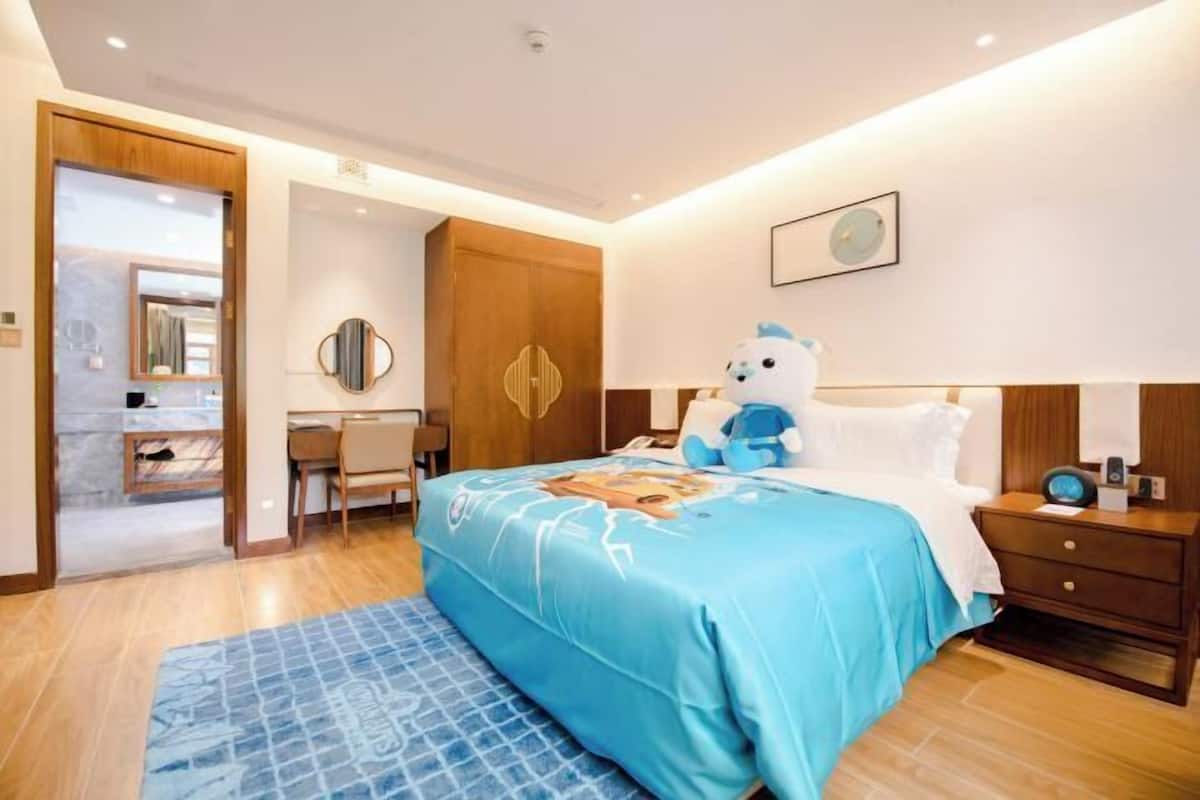 Une chambre d’hôtel comprenant un lit, un bureau, une chaise, une table de chevet et une horloge murale.