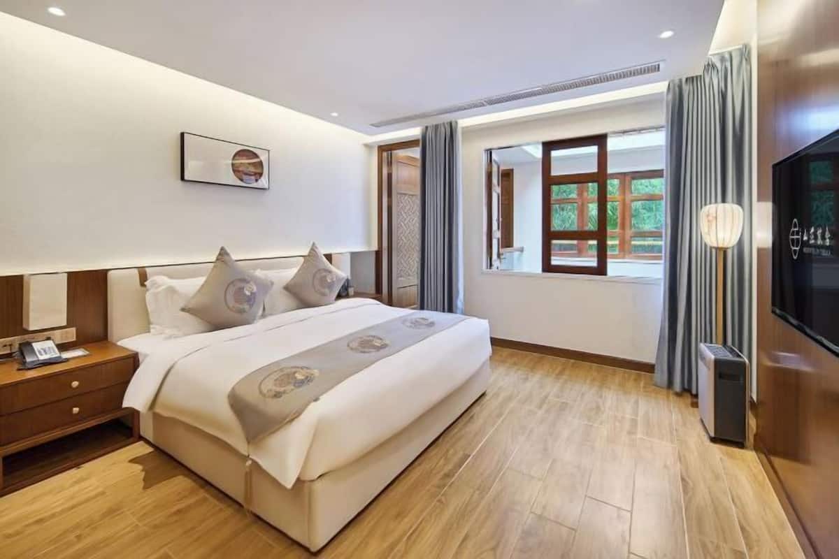 Une chambre d’hôtel moderne avec un grand lit, une table de chevet, une télévision et une fenêtre avec des rideaux.