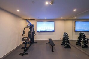 Et træningscenter med træningsudstyr, en bænk og et tv-skærm.