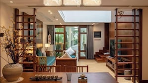 Un vaste espace de vie comprenant une table à manger en bois, un canapé et un téléviseur. Un escalier mène à un balcon, et une grande fenêtre offre une vue sur l’extérieur.