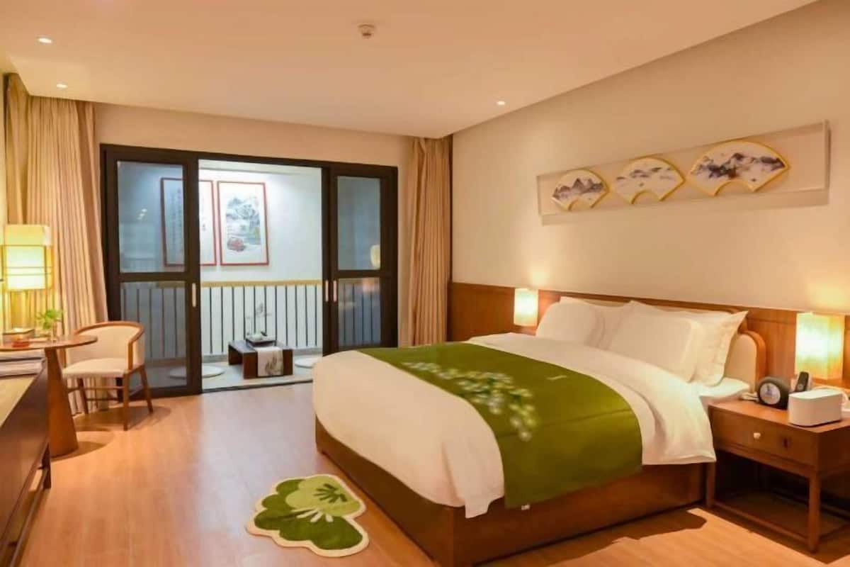 Une chambre d’hôtel avec un lit, une table de chevet, une lampe, une chaise et une vue sur l’extérieur, visible à travers une porte vitrée.