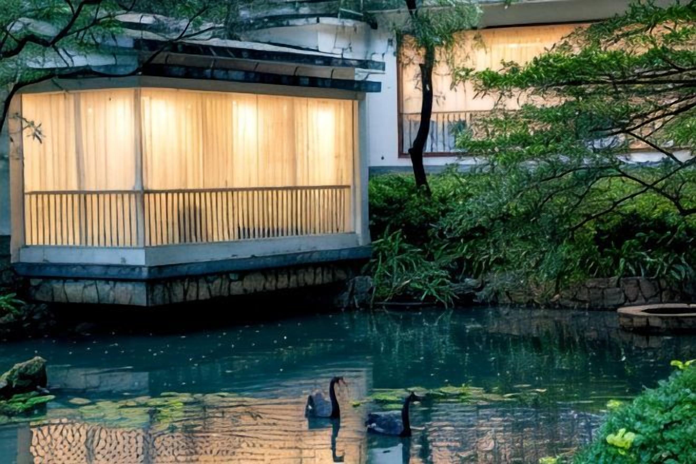 A serene indoor garden with a pond, a wooden structure with a view, and lush greenery.