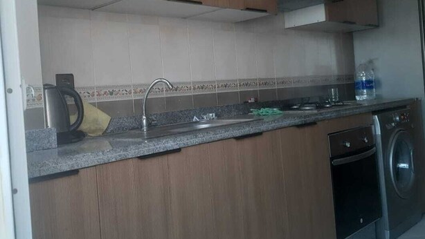 Een keuken met houten kastjes, een roestvrijstalen spoelbak, een waterkoker, een wasmachine en een betegelde spatwand.