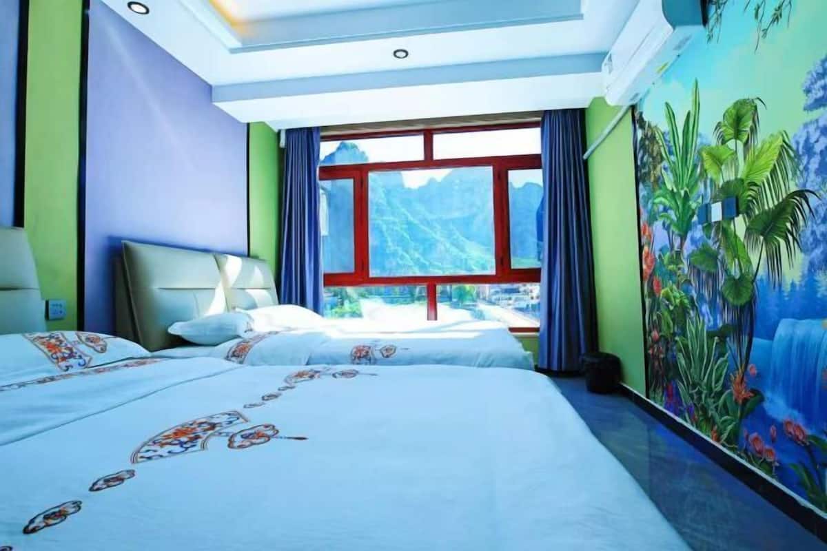 A hotel room with two beds, a large window, and a mural of a waterfall.