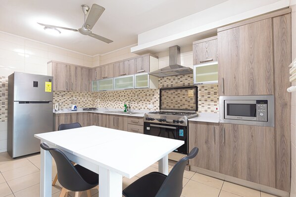 A modern kitchen with a white table, black chairs, a stainless steel refrigerator, a microwave, and a stove. - Elite Apartment (Accra)
