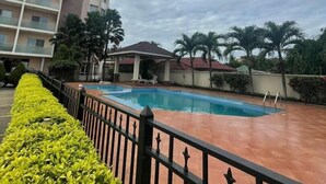 Una piscina con borde de baldosas, rodeada por una cerca baja y frondosos arbustos verdes.