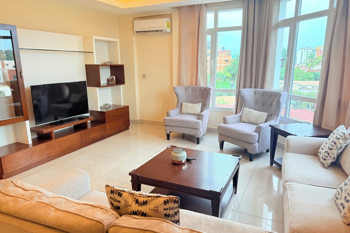 A modern living room with a flat-screen TV, two armchairs, a sofa, and a coffee table.