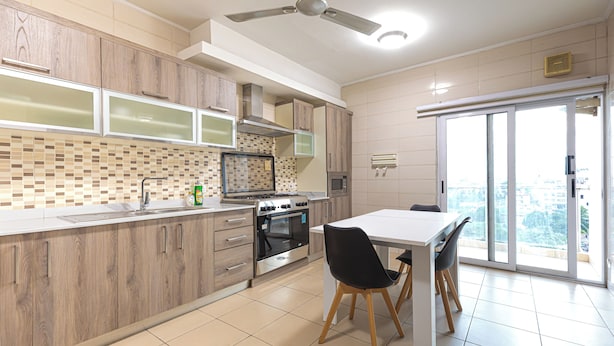 Una cocina moderna con armarios de madera, horno empotrado y comedor con mesa blanca y sillas negras.