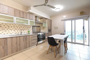 A modern kitchen with wooden cabinets, a built-in oven, and a dining area with a white table and black chairs. - Elite Apartment (Accra)