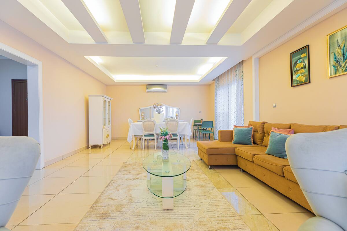 A spacious living room with a glass coffee table, a sofa, and a dining area with a table and chairs.