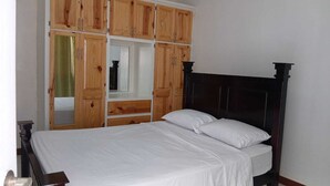 A bedroom with a bed, wooden wardrobe, and a dark headboard. - Quiet and spacious 2-bedroom apartment with AC, WiFi in exciting Turkeyen (Turkeyen)