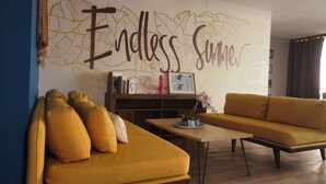 A living room with a mustard sofa, a coffee table, and a wall with 'Endless Summer' written on it. - Hotel Montañita (Montañita)