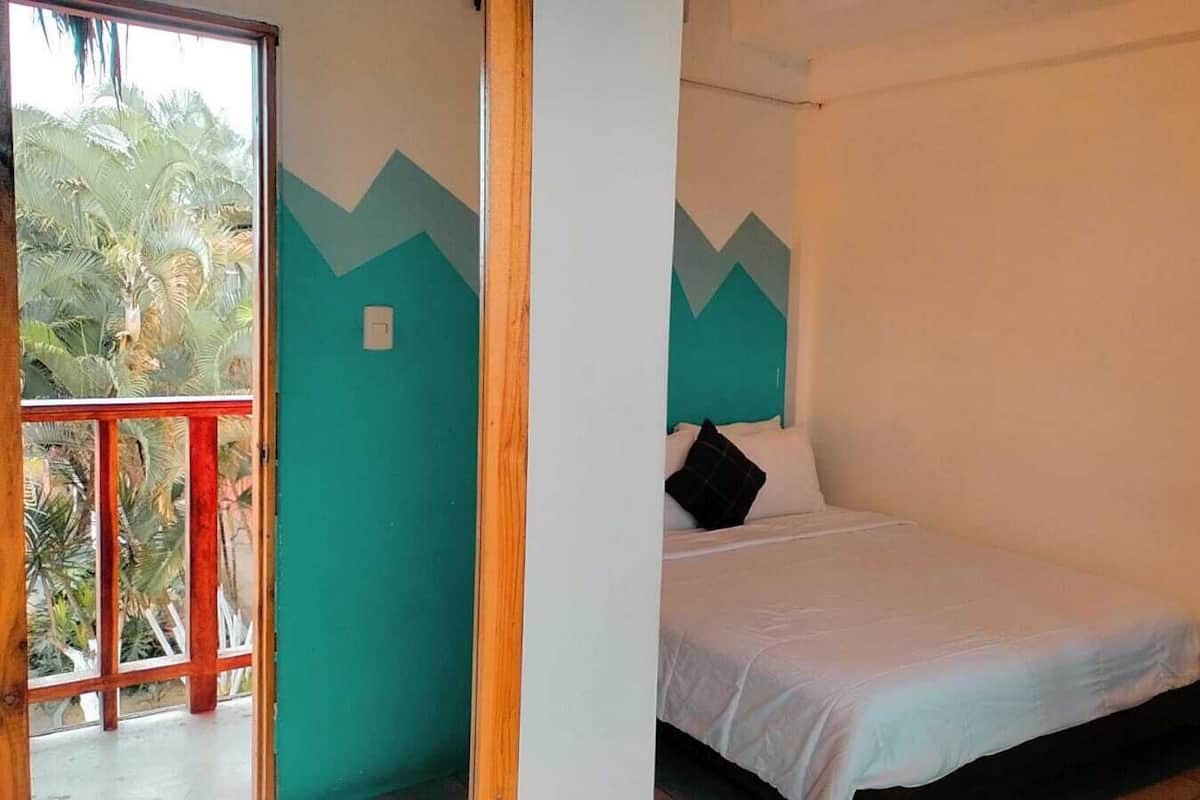 A single bed with white bedding in a room with teal walls and a window overlooking palm trees.