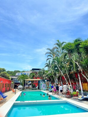 A swimming pool with people around it, surrounded by palm trees and buildings. - Hotel Montañita (Montañita)