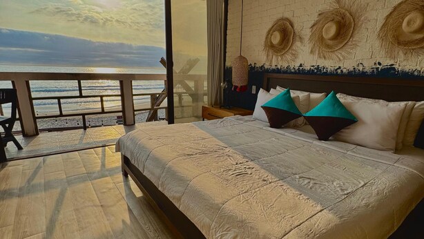 A bedroom with a large bed, a ceiling fan, a view of the ocean, and a brick wall with decorative hats. - Hotel Montañita (Montañita)