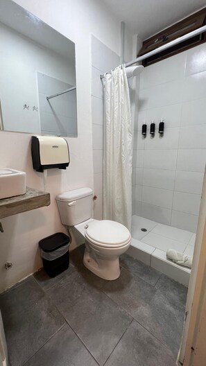A bathroom with a toilet, a sink, a shower with a curtain, and a hand dryer. - Hotel Montañita (Montañita)