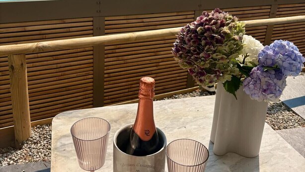 Escena junto a la piscina con una botella de champán, dos copas y un florero.